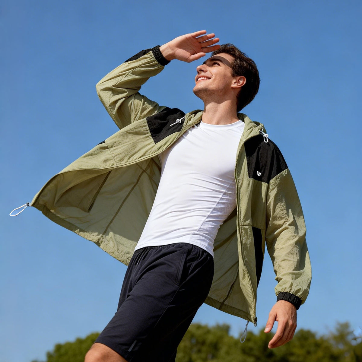 Venzina Sunscreen Jacket for Men worn outdoors, low-angle pose with raised hand, olive-black jacket open, blue sky backdrop