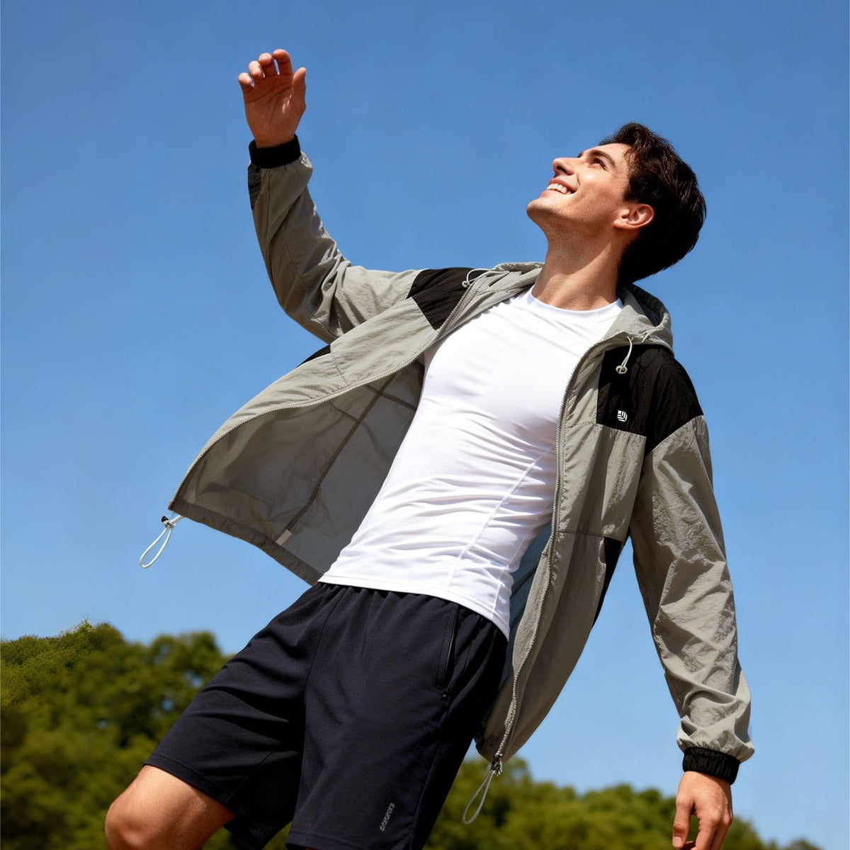 Venzina sun protective clothing worn outdoors, low-angle action shot in grey-black hooded jacket, blue sky and trees