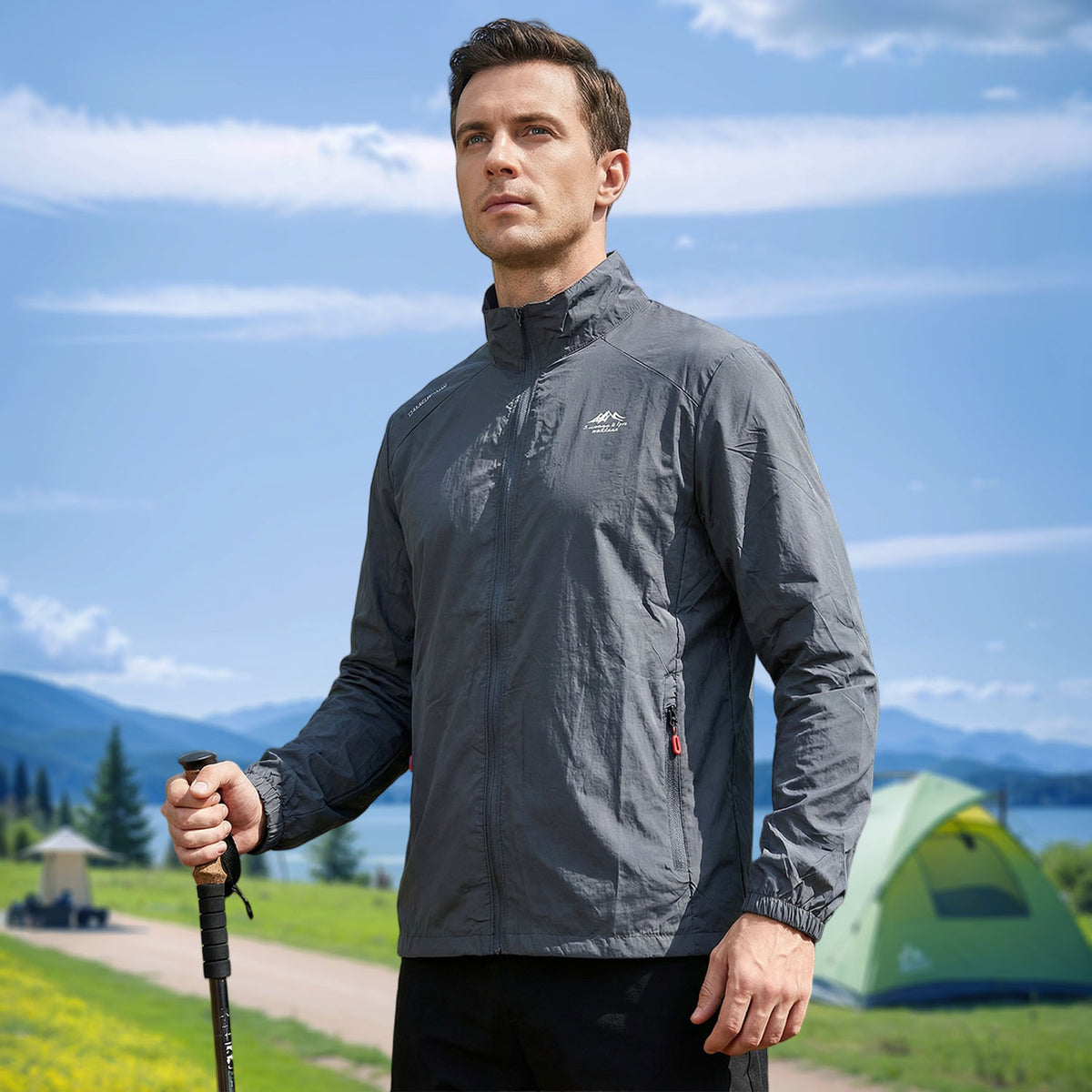 Venzina sunscreen jacket in grey worn hiking, three-quarter view with trekking pole, tent and mountains