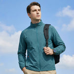 Venzina sunscreen jacket in teal worn outdoors, front three-quarter view with backpack strap against blue sky