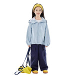 Girl wearing a light blue kids outdoor jacket with hood, navy pants, and yellow bag — breathable windbreaker jacket for everyday wear.