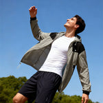 Venzina sun protective clothing worn outdoors, low-angle action shot in grey-black hooded jacket, blue sky and trees