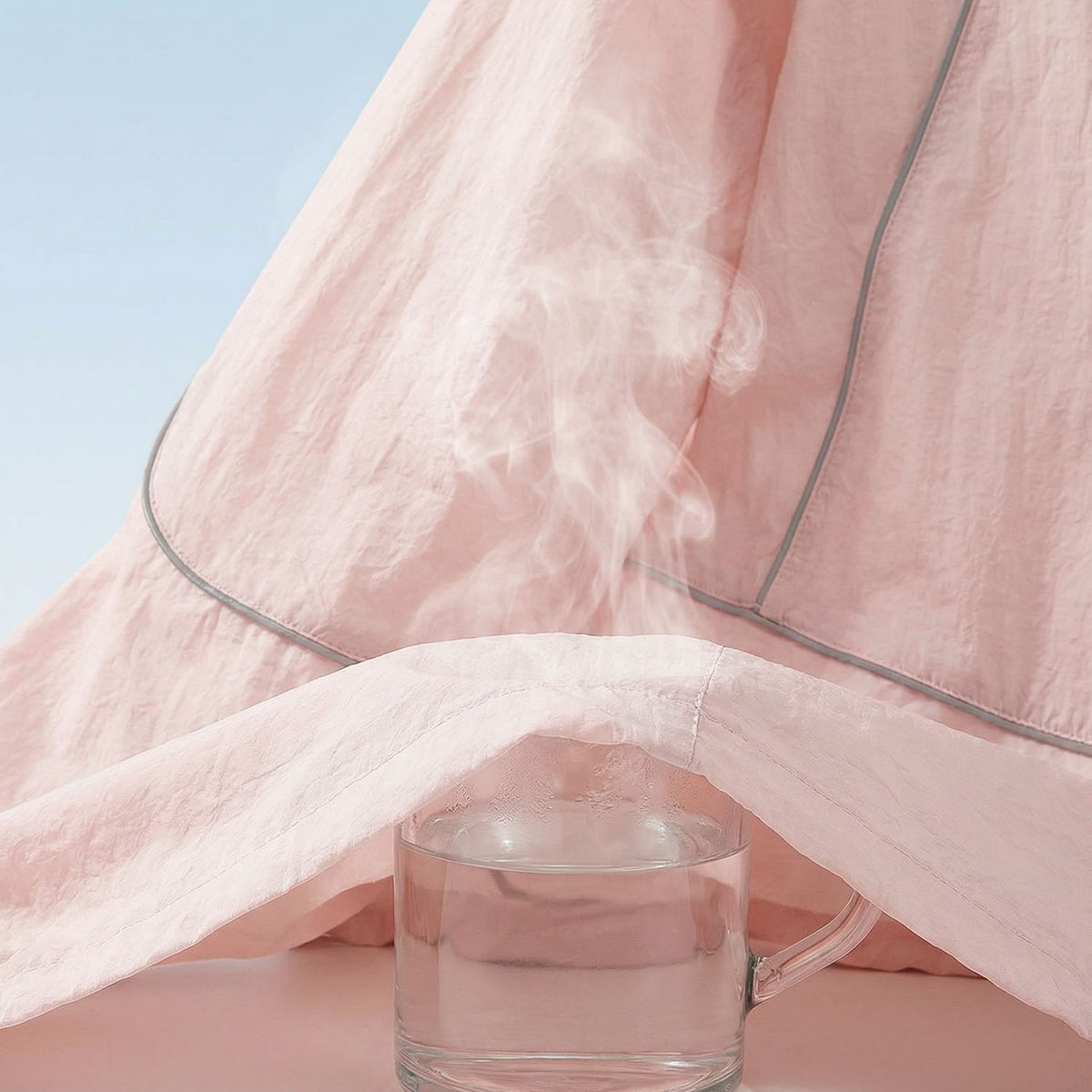 Venzina sun protective jacket close-up, pink fabric draped over steaming glass mug, seam piping detail
