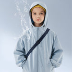 Girl wearing a light blue water-resistant kids outdoor jacket with hood — breathable windbreaker jacket showing splash-proof fabric test.